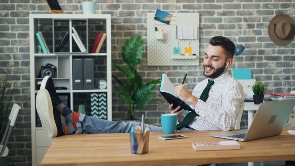 Relaxed young man in office with notebook and laptop, embodying modern work culture.